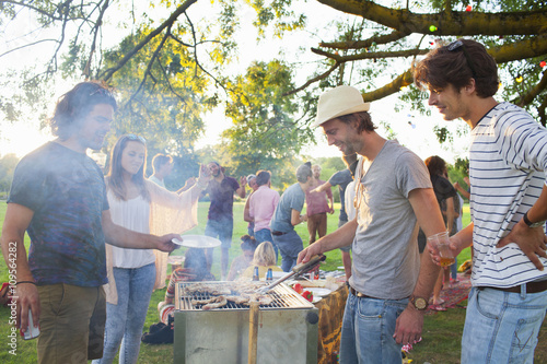 Happy adult friends barbecuing at sunset party in park