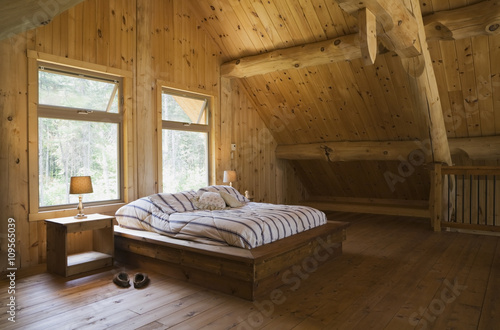 King size bed with wooden bed frame in the master bedroom, on mezzanine inside a handcrafted Eastern white pine cottage style log home, Quebec, Canada photo