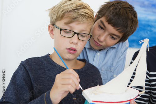 Teenage boy and brother painting toy boat at kitchen table photo