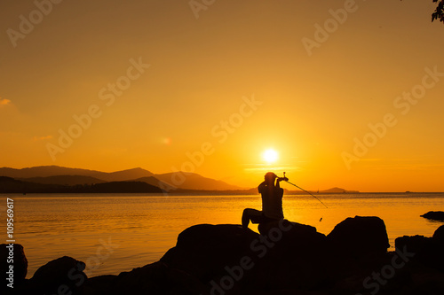 Young man sitting on the stone play smartphone at sea 