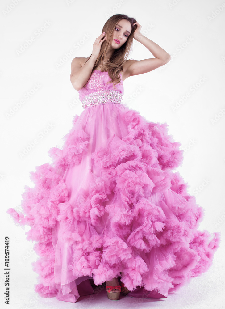 Fototapeta premium Portrait of young beautiful caucasian blonde in gorgeous pink dress on white background