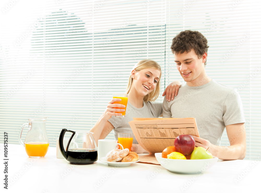 Young casual couple have breakfast with coffee and fruit newspaper with venetian blind window Young casual couple have breakfast with coffee and fruit newspaper with venetian blind window