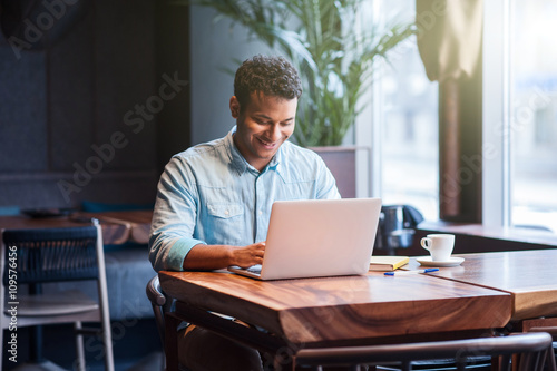 Attractive male worker is using computer in cafeteria 