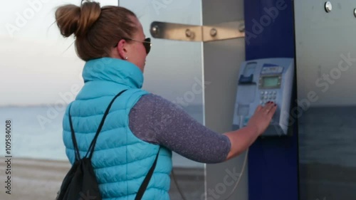 Beautiful girl picks up the phone dials the number of a payphone on the street