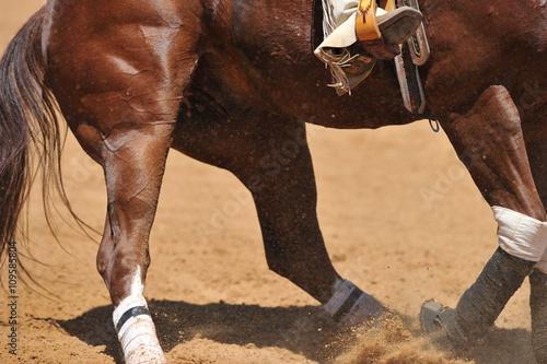 View of the sliding in the dust horse and rider foot with boots and spurs in the stirrup during the riding