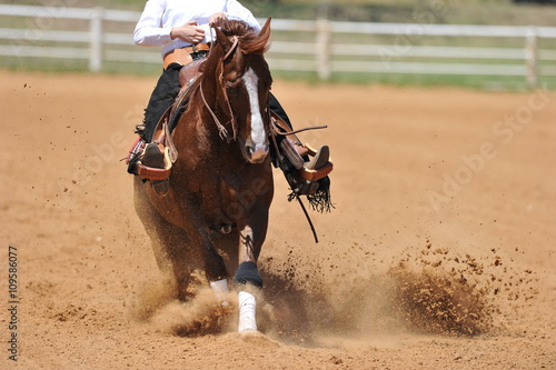 A front view of a rider and horse sliding in the dust.