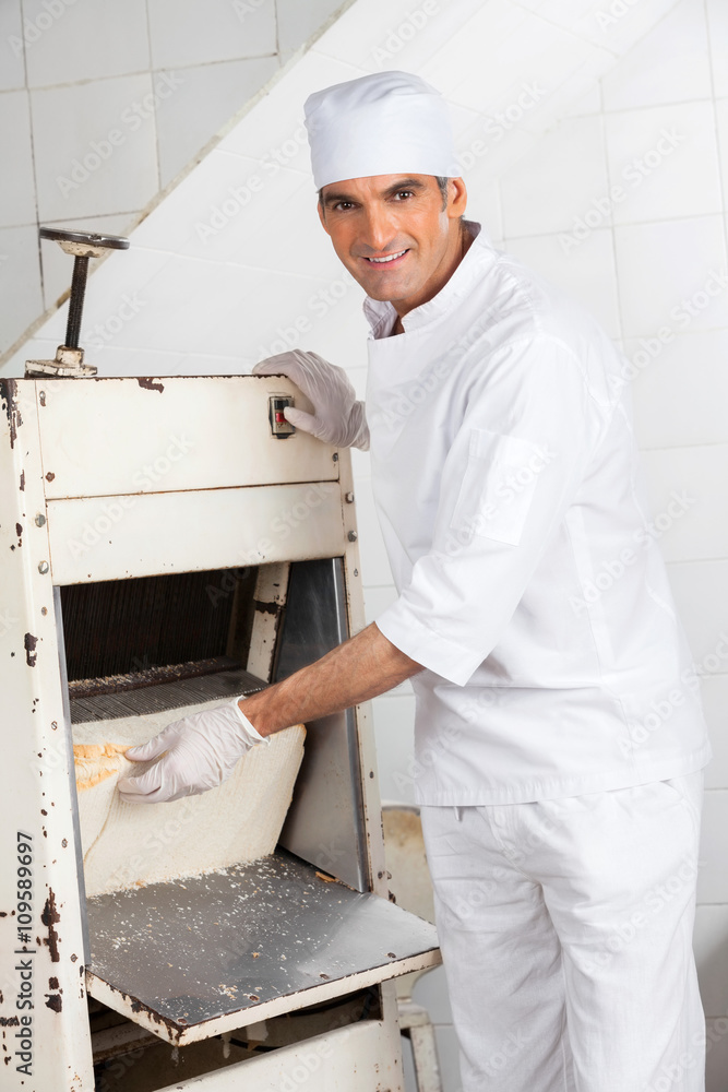 Male Baker Using Bread Slicer At Bakery