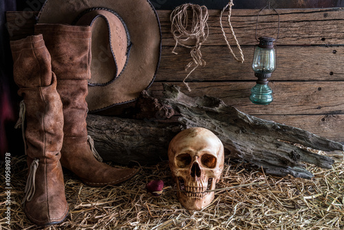 Still life human skull and rose on hay with traditional leather boots and ame...
