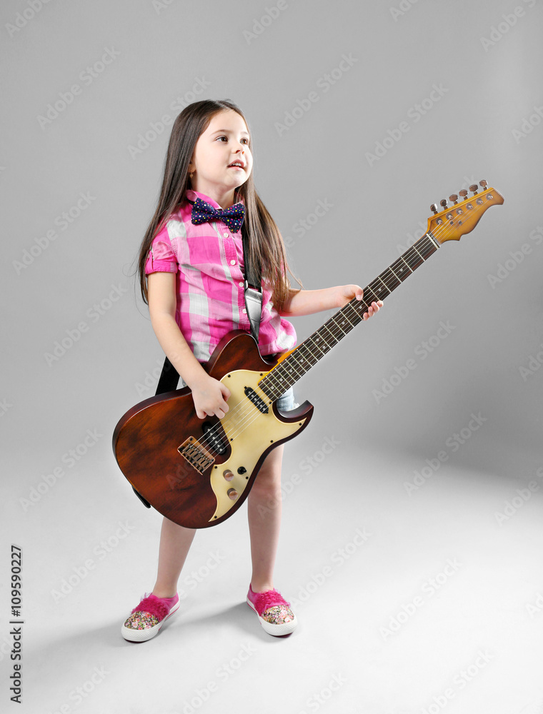Beautiful artistic little girl playing guitar on grey background Beautiful artistic little girl playing guitar on grey background
