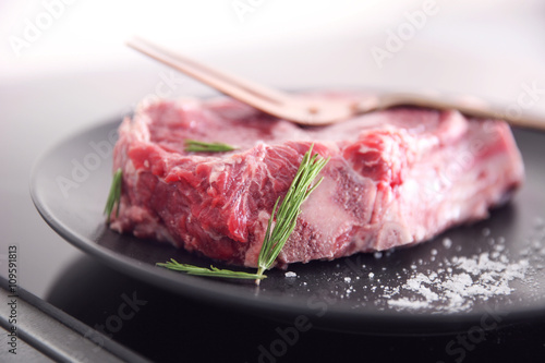 Raw pork steak with meat fork and rosemary on black plate