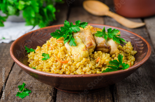 Chicken bulgur pilaf in clay bowl on wooden background. Selective focus