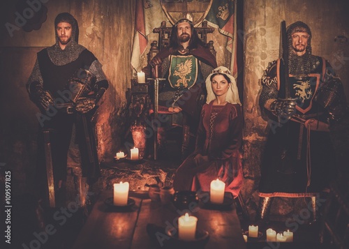 Photography Medieval king with his queen and knights on guard in ancient castle interior