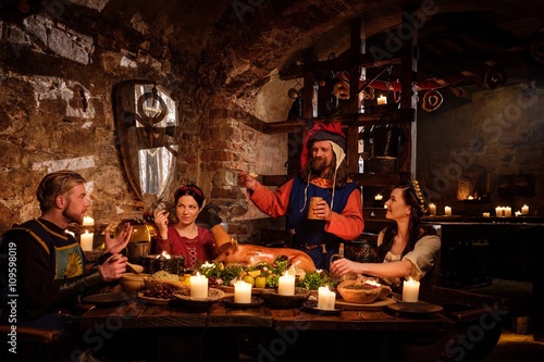 Bilde på lerret Medieval people eat and drink in ancient castle kitchen interior.