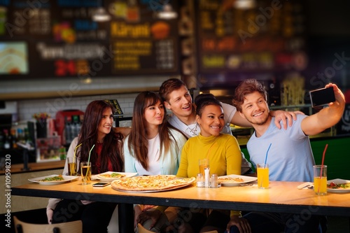 Cheerful multiracial friends taking selfie in pizzeria.