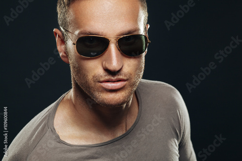 Handsome man wearing sunglasses in the studio on a dark backgrou © djile
