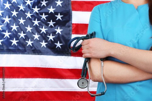 Female doctor holding in hand stethoscope with USA flag on background