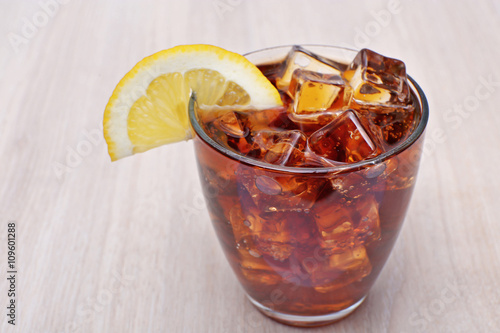 Glass of cola with ice on light wooden background