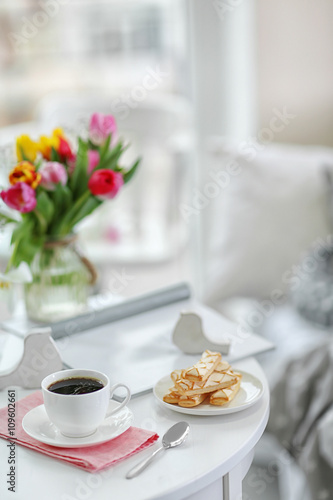 White cup of the coffee and sweets on wooden table  in a light room..