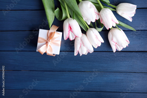 Bouquet of fresh tulips and present box on blue wooden background