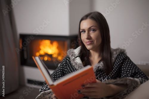 Portrait of beautiful woman reading book by fireplace