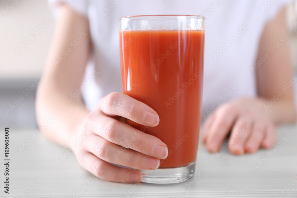 Female hand holding glass of tomato juice on wooden table closeup Female hand holding glass of tomato juice on wooden table closeup
