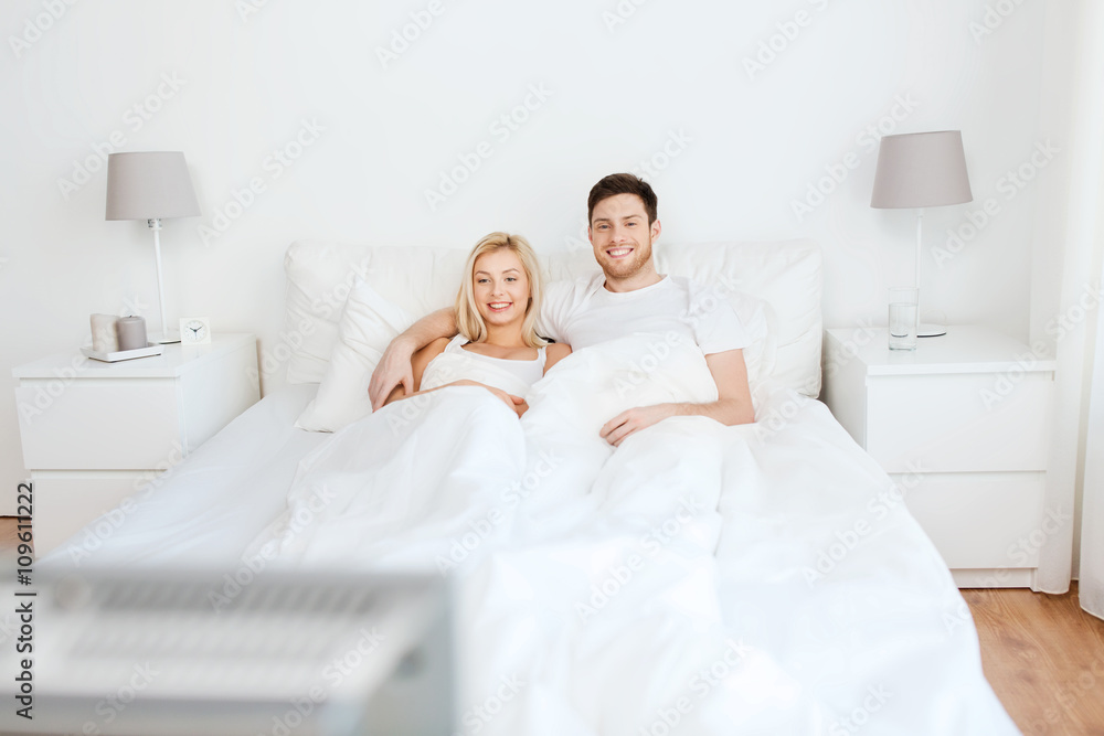 happy couple lying in bed at home and watching tv happy couple lying in bed at home and watching tv