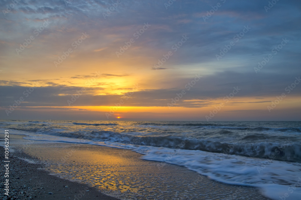 Colorful sunrise on the sea coast, waves, foam