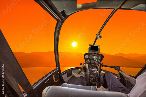 Helicopter cockpit on the sea at sunset, with pilot arm and control board inside the cabin