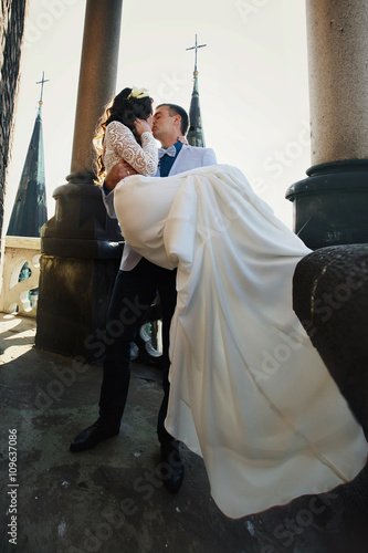 Fiance holds bride in his arms on the rooftop of old cathedral