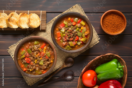 Vegan goulash made of soy meat (textured vegetable protein), capsicum, tomato and onion served in rustic bowls, photographed overhead on dark wood with natural light