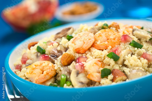 Couscous dish with shrimps, mushroom, almond, pomegranate seeds and green onion served in blue bowl (Selective Focus, Focus on the tails of the shrimps on the top of the meal)