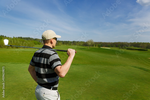male golfer relaxes at fairway during a sunny day, back view