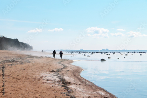 Two bikers are riding along the sea coastline on the deserted misty beach.