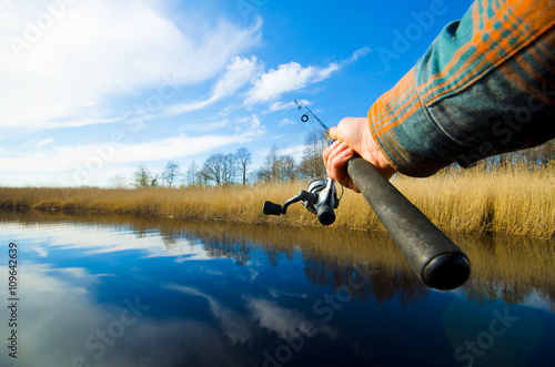 Fisherman start to fishing by spinning on the river in sunny weather. Fishing process. Eye view