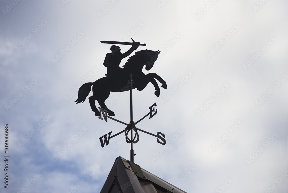 metal weather vane in a shape of knight on horse on a rooftop