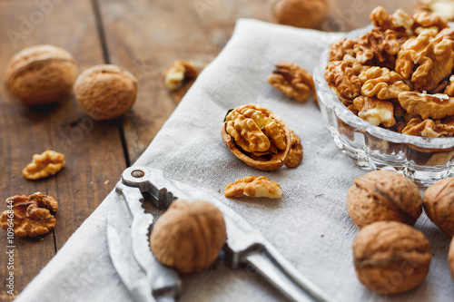 Glass bowl with walnuts on rustic homespun napkin. Healthy snack on old wooden background.