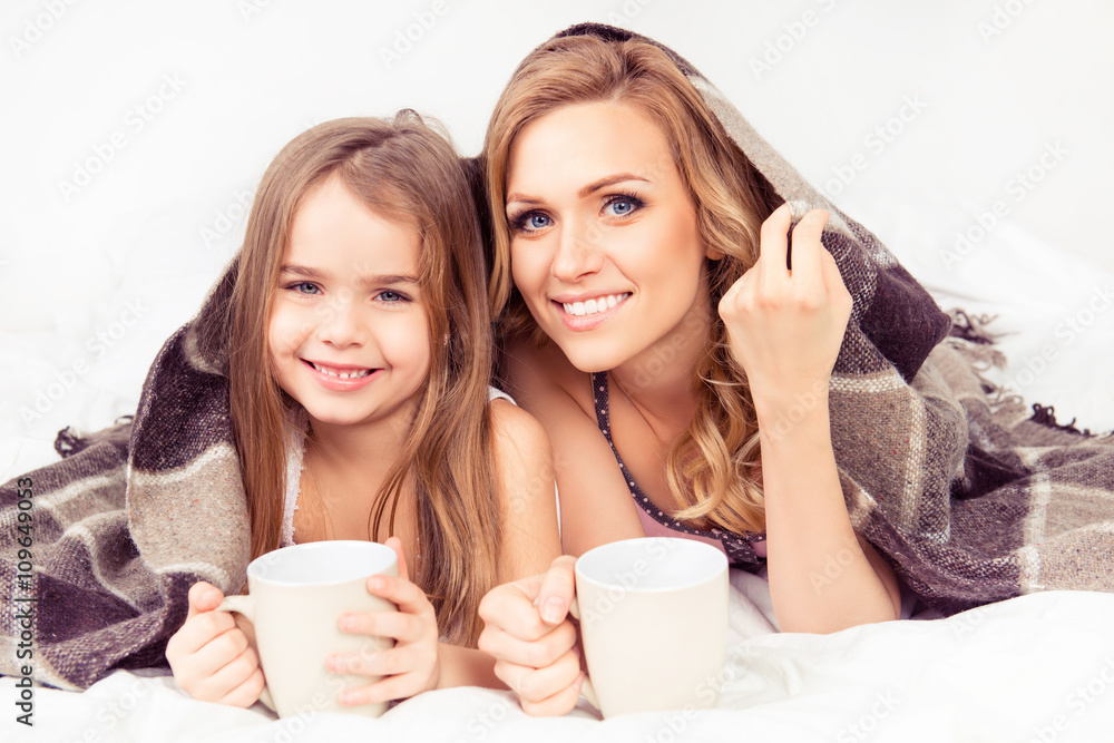 Portrait of mom and daughter basking under plaid with cups of ho Portrait of mom and daughter basking under plaid with cups of ho