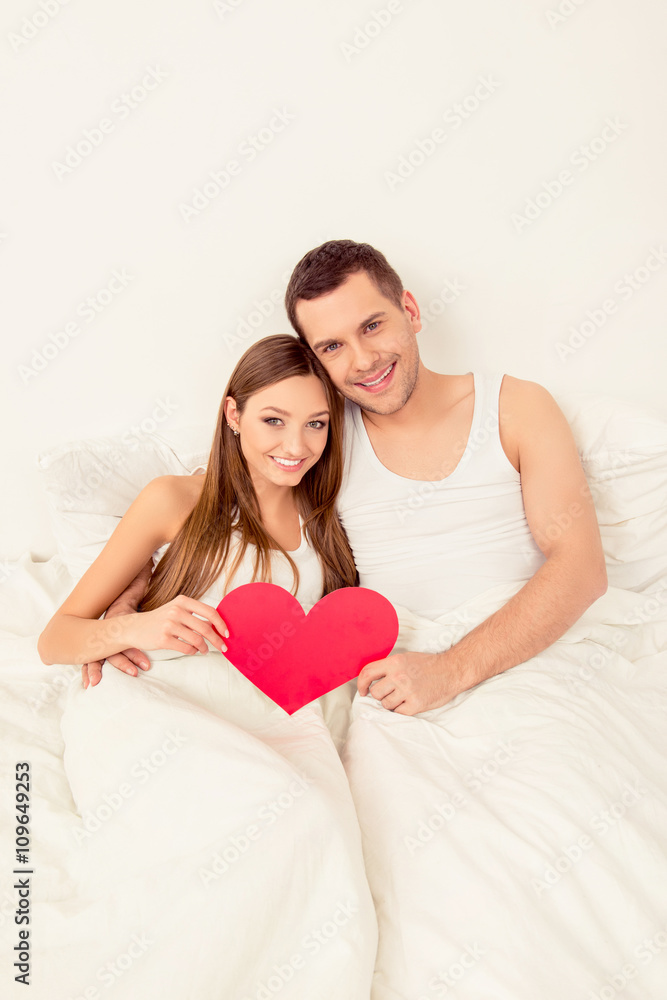 Couple in love lying in bed with big paper heart