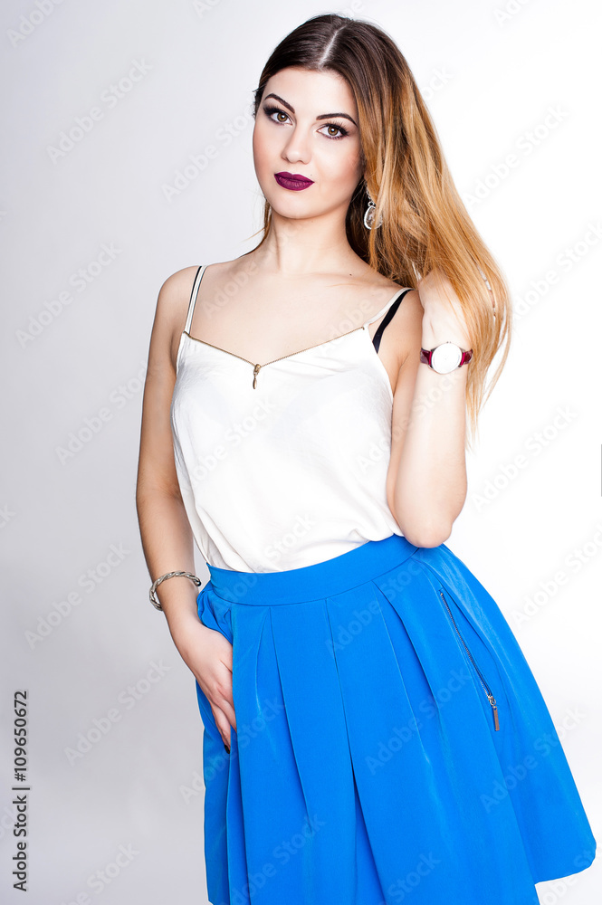Bright positive fashion studio portrait of pretty young girl with purple lips, bright make up, sexy body, stylish trendy outfit: blue skirt, smart casual, cute emotions, color pop, white background. Bright positive fashion studio portrait of pretty young girl with purple lips, bright make up, sexy body, stylish trendy outfit: blue skirt, smart casual, cute emotions, color pop, white background.