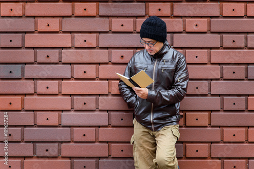 An Asian Man in a Brown Jacket with a Small Notebook Fototapeta