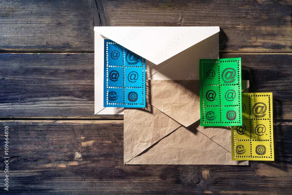 Fototapeta premium Postage stamp with e-mail sign and an envelope lying on an old wooden surface.