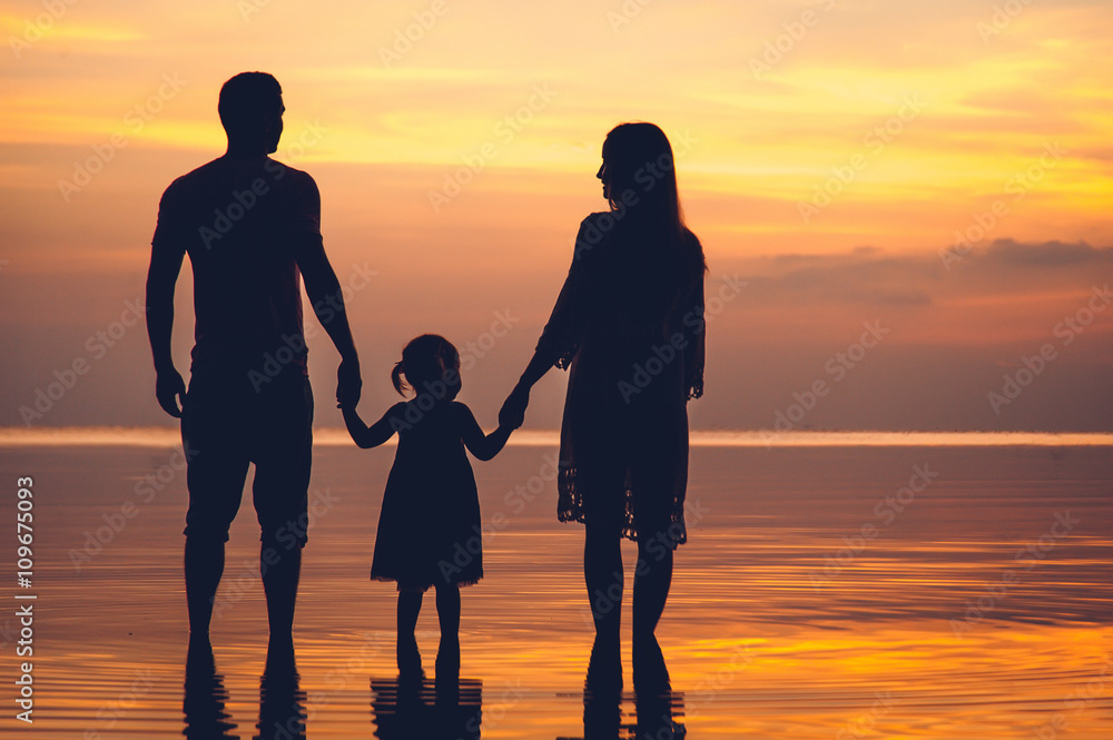 Silhouette of two adults and a child at the beach on sunset