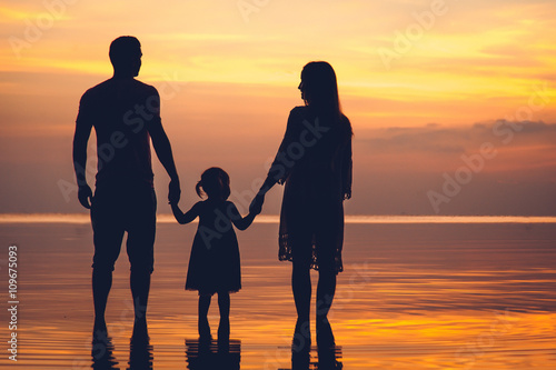 Silhouette of two adults and a child at the beach on sunset