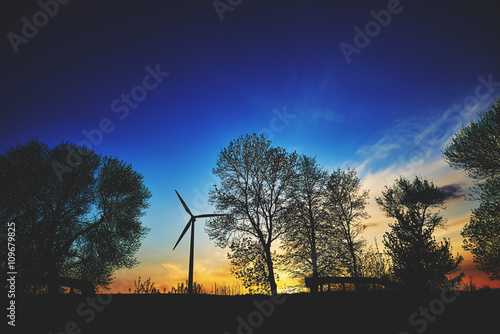Elektrownia wiatrowa na tle wieczornego nieba pomiędzy drzewami