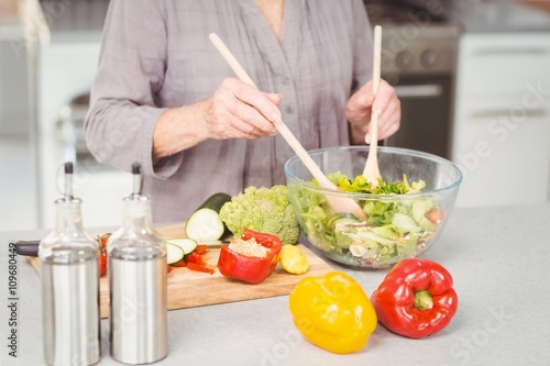 Midsection of woman preparing salad while standing at kitchen counter