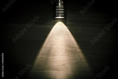 Flashlight and a beam of light in darkness. A modern led light with bright projection on dark wood table. Surface with copy space. photo