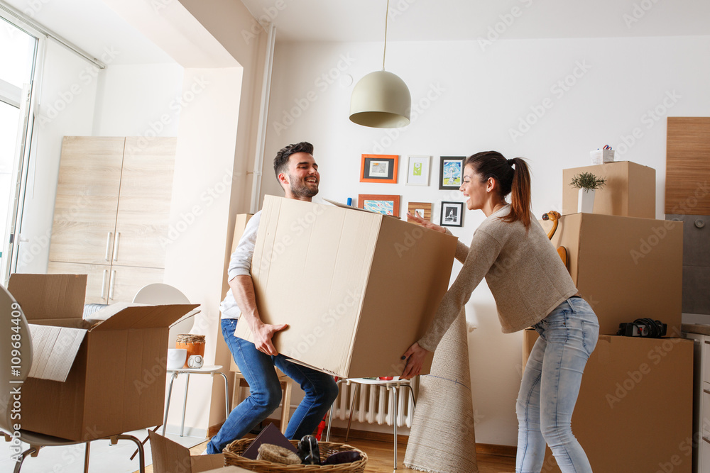 Young couple carrying big cardboard box at new home.Moving house. - obrazy, fototapety, plakaty 