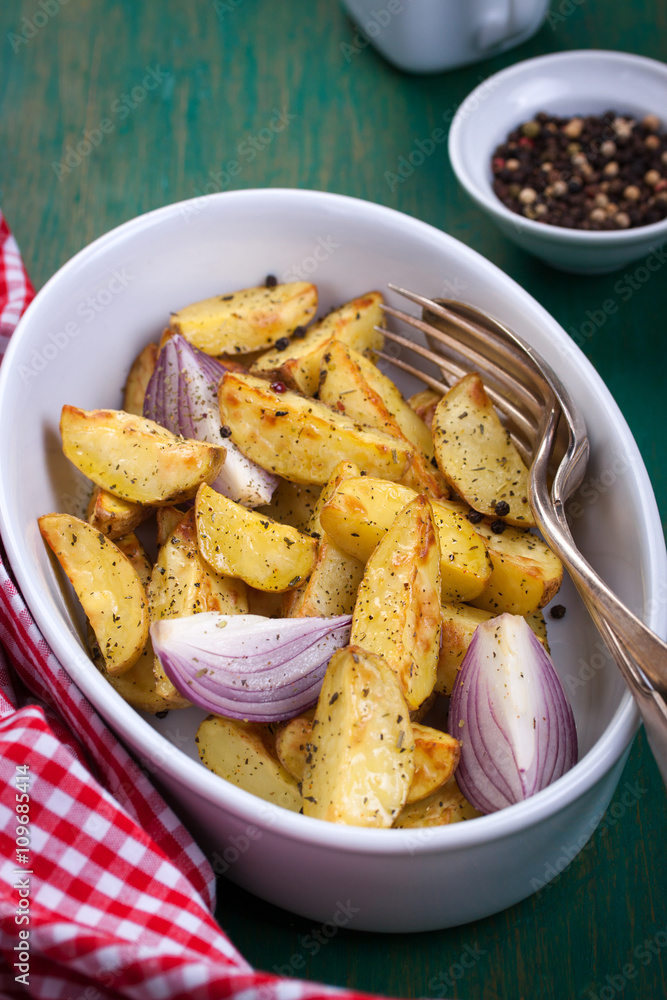Oven-baked cut potato with red onion and Italian herbs, rustic, vintage or country style in a round bowl with red napkin on an old vintage green wooden background, closeup Oven-baked cut potato with red onion and Italian herbs, rustic, vintage or country style in a round bowl with red napkin on an old vintage green wooden background, closeup