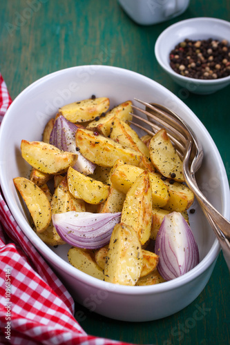 Oven-baked cut potato with red onion and Italian herbs, rustic, vintage or country style in a round bowl with red napkin on an old vintage green wooden background, closeup