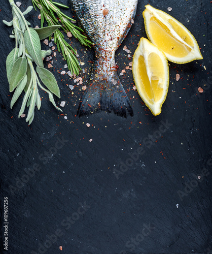 Tail of fresh raw Dorado or sea bream fish on black slate stone board with spices, herbs, lemon and salt photo